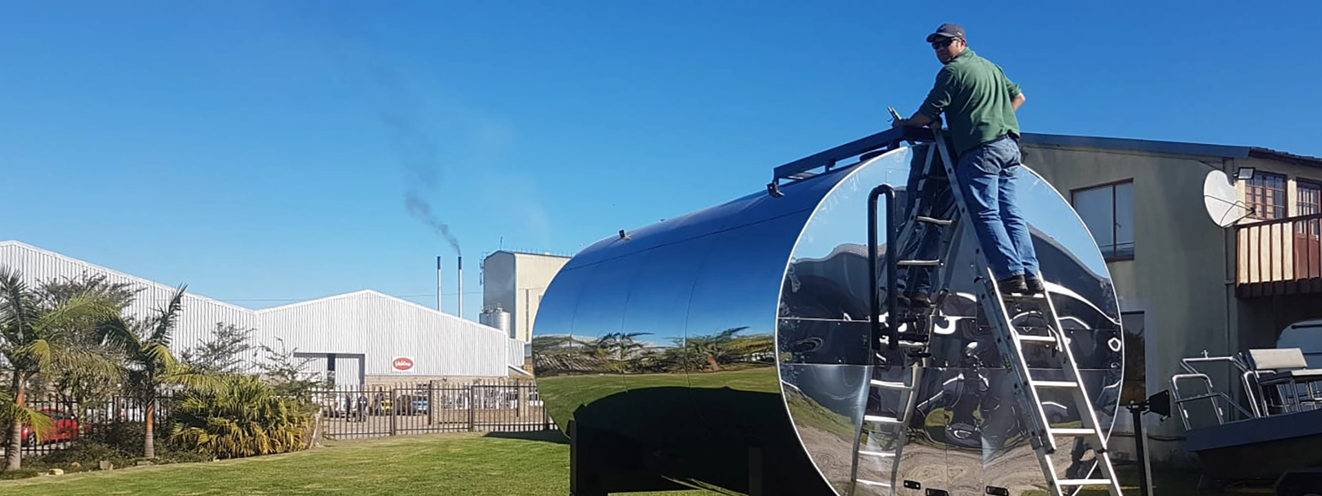 A BMD Engineering technician climbing a ladder to inspect a mirror-polished stainless steel hotwell tank mounted on a trailer, with an industrial facility visible in the background.